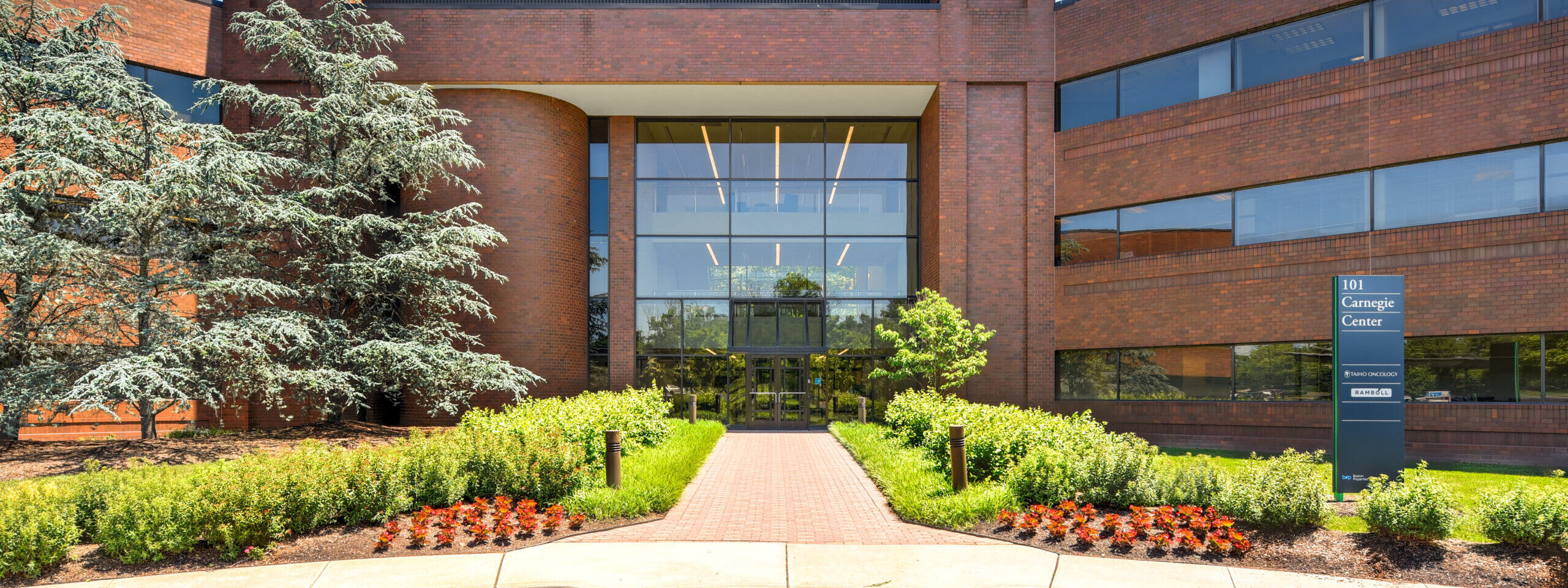 Exterior shot of a brick office building entrance with walkway lines with plantings.