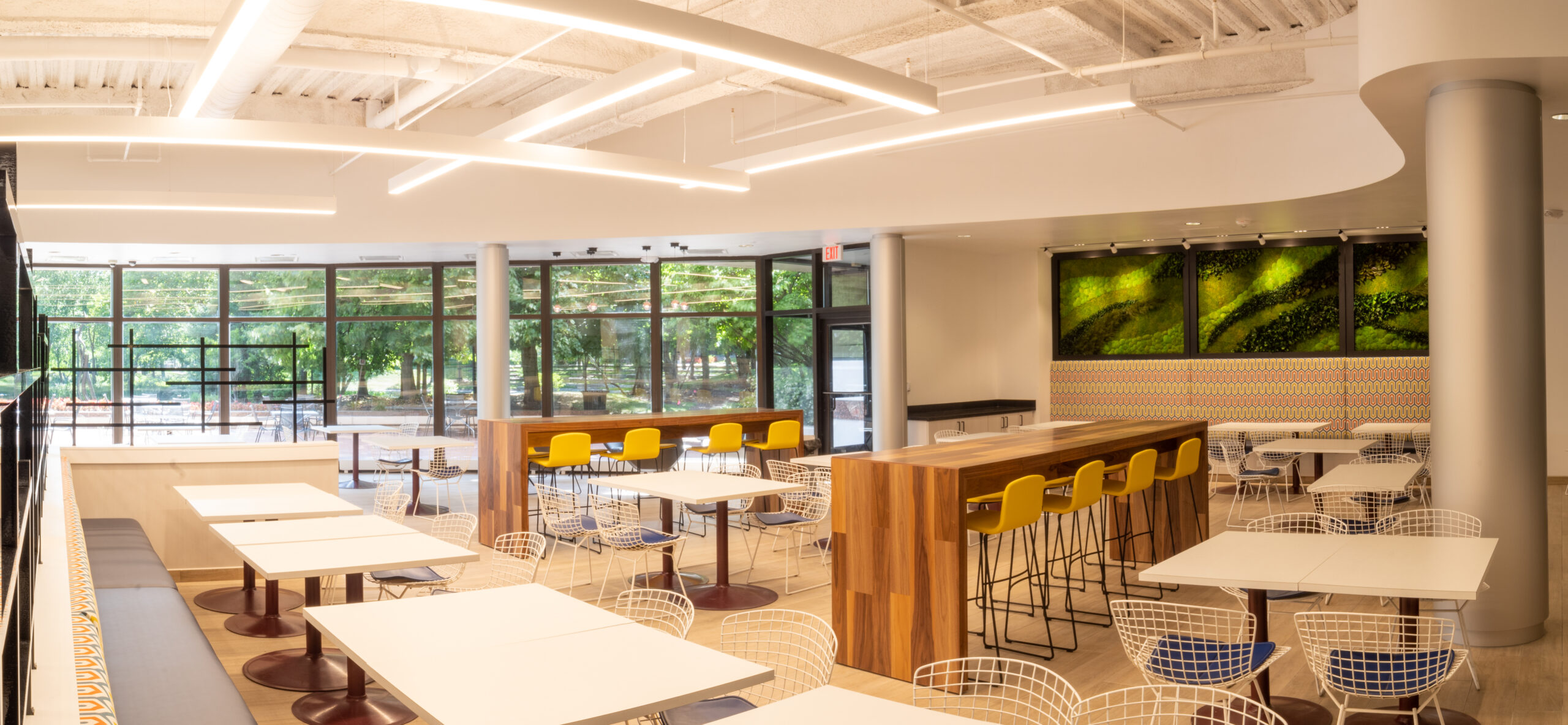 An open cafe seating area, featuring high top and low top tables with pops of wood accents and greenery.