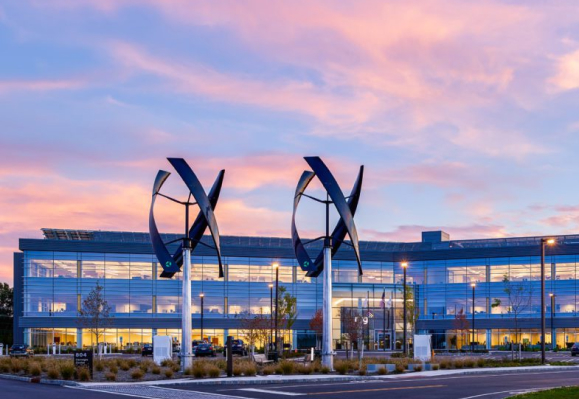 Exterior view of an office building at dusk with two wind turbines below a blue and pink sky.